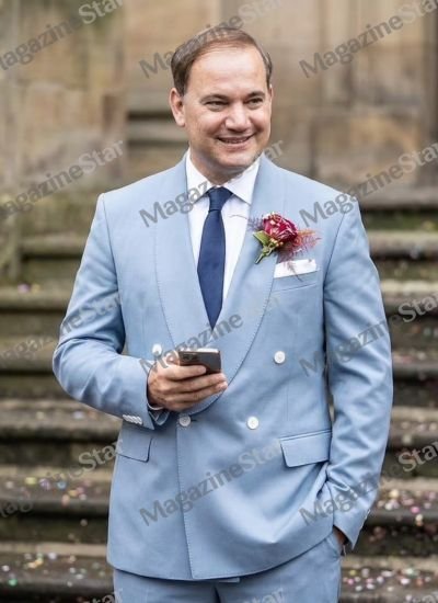 Reinaldo Avila da Silva wearing a light blue double breasted suit holding a phone at a wedding event