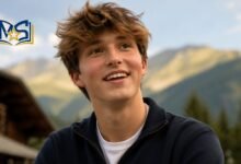 A smiling portrait of professional downhill racer Oscar Griffiths, the eldest son of actress Gillian Anderson, against a mountain landscape background.