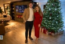 A couple posing beside a decorated Christmas tree in a modern living room.