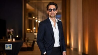 Hugo Taylor wearing a navy suit and sunglasses at an indoor event